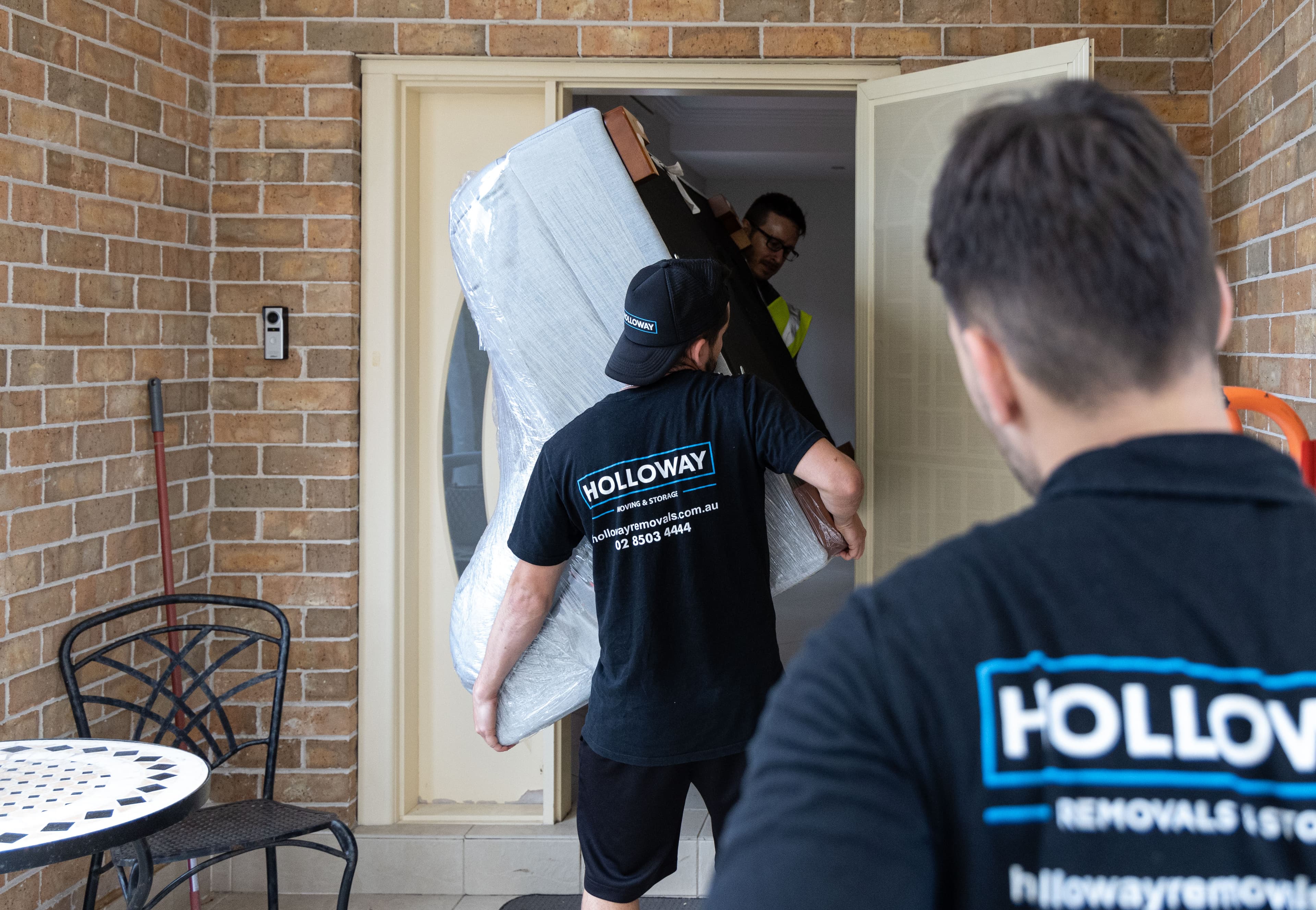 Removalists Moving Wrapped Furniture Outside a House